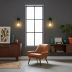 Black-finish Clérachic wall lights flank a tall window in a dark grey room with a walnut sideboard and orange armchair.
