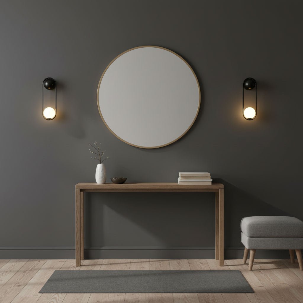 Black-finish Clérachic wall lights flank a round mirror above a wooden console table on a dark charcoal wall.