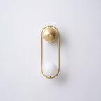 A brass Clérachic wall light on a plain wall, its opal glass globe shown unlit and its shadow visible beside it.