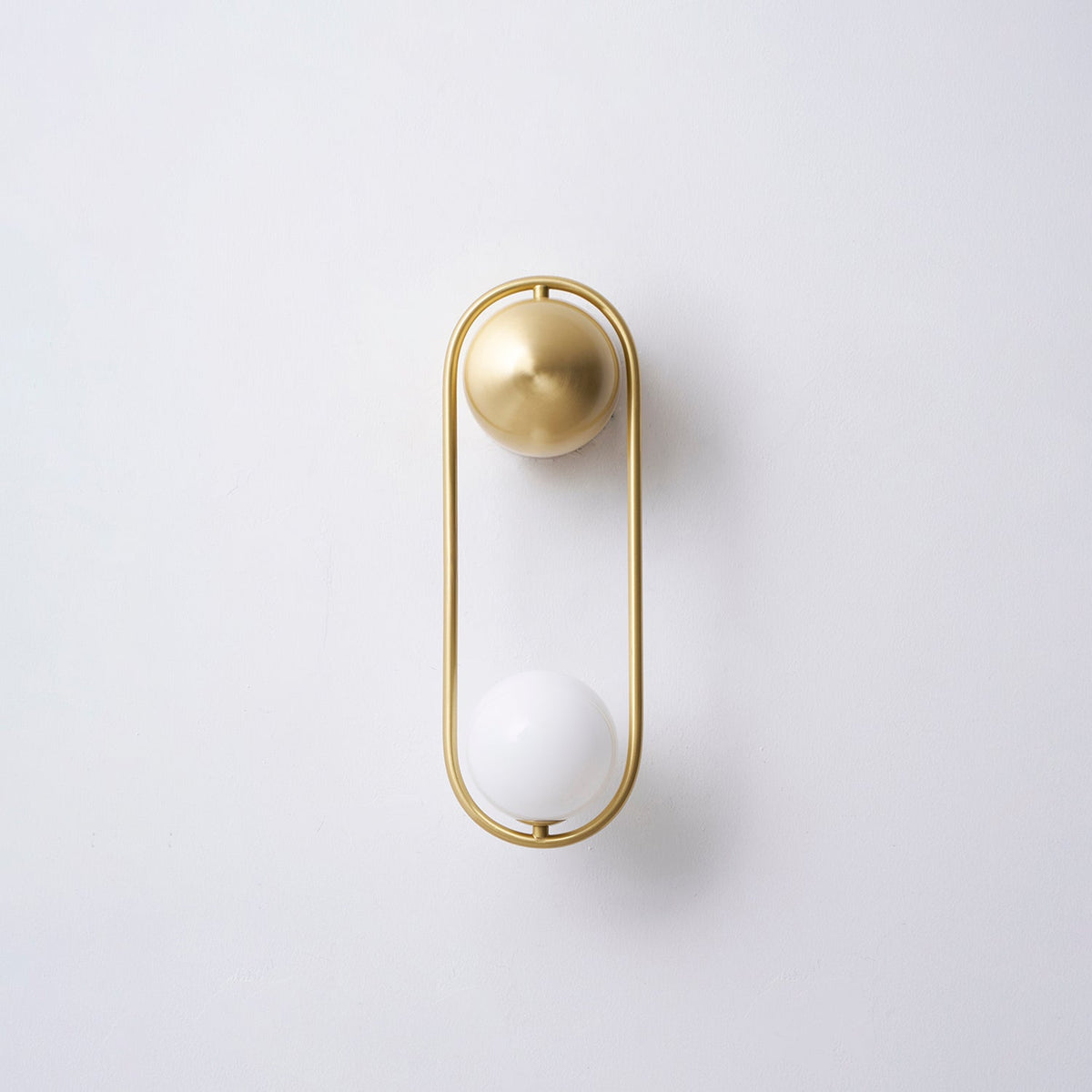 A brass Clérachic wall light on a plain wall, its opal glass globe shown unlit and its shadow visible beside it.