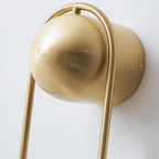 Extreme close-up of the matte brass ball top on this Clérachic wall light against a plain wall, shown unlit.