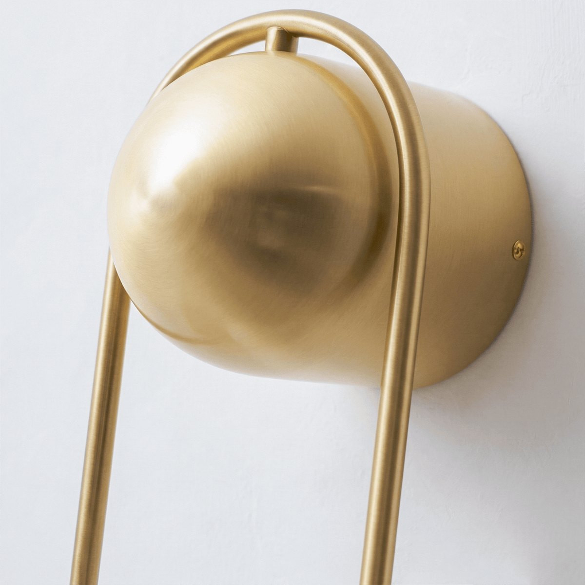 Extreme close-up of the matte brass ball top on this Clérachic wall light against a plain wall, shown unlit.