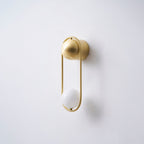 Angled view of this brass Clérachic wall light on a plain wall, its opal glass globe unlit and casting a soft shadow.