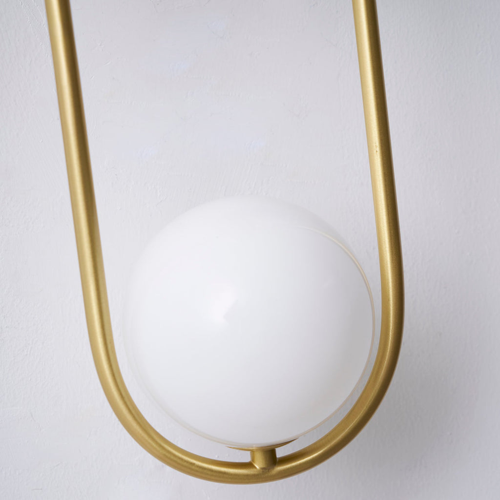 Extreme close-up of the opal glass globe at the base of this Clérachic wall light, shown unlit against a plain wall.