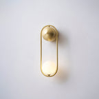 This brass Clérachic wall light on a plain wall, its opal glass globe glowing warm at the base of the loop.