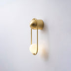 Angled view of this brass Clérachic wall light on a plain wall, its opal glass globe glowing warm.