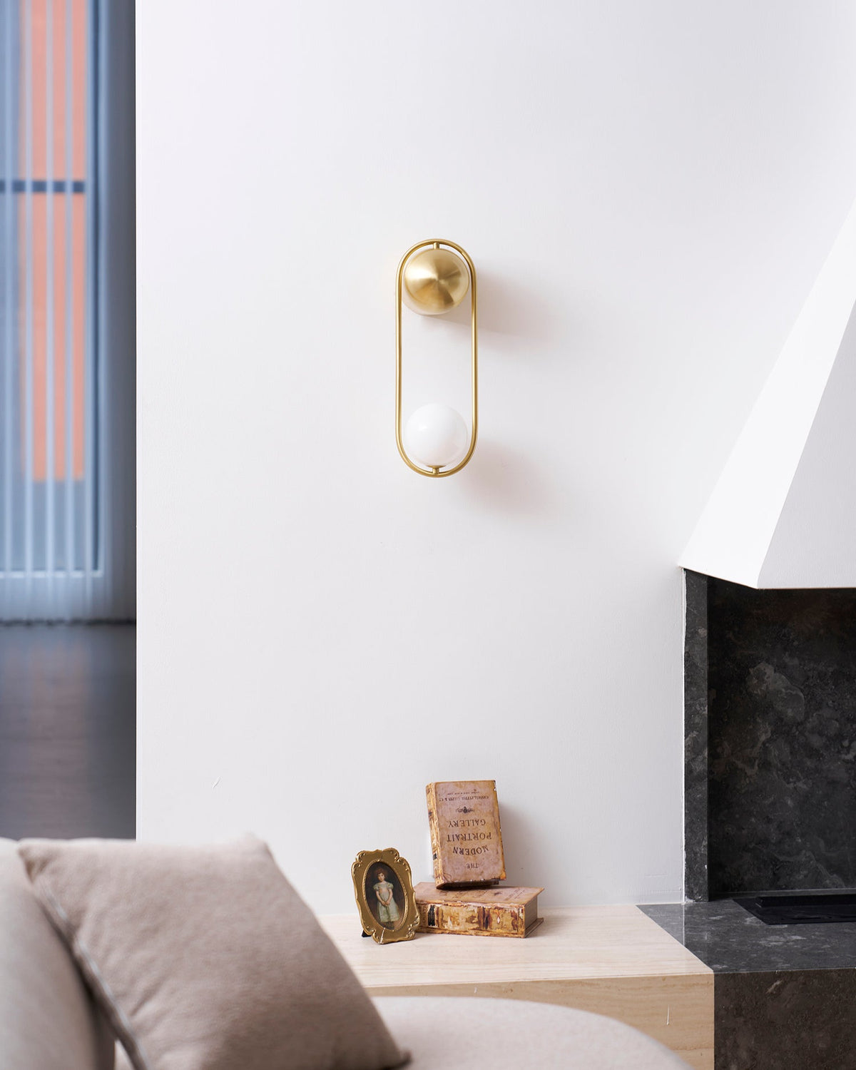 In a room with a fireplace and small framed photos on the hearth, this brass Clérachic wall light sits on a plain wall.