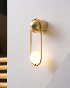 Against a wall with a dark triangular shadow, this brass Clérachic wall light glows warm through its opal glass globe.