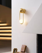 Beside a sunlit stairwell with warm light streaking the wall, this brass Clérachic wall light glows above a small framed photo.