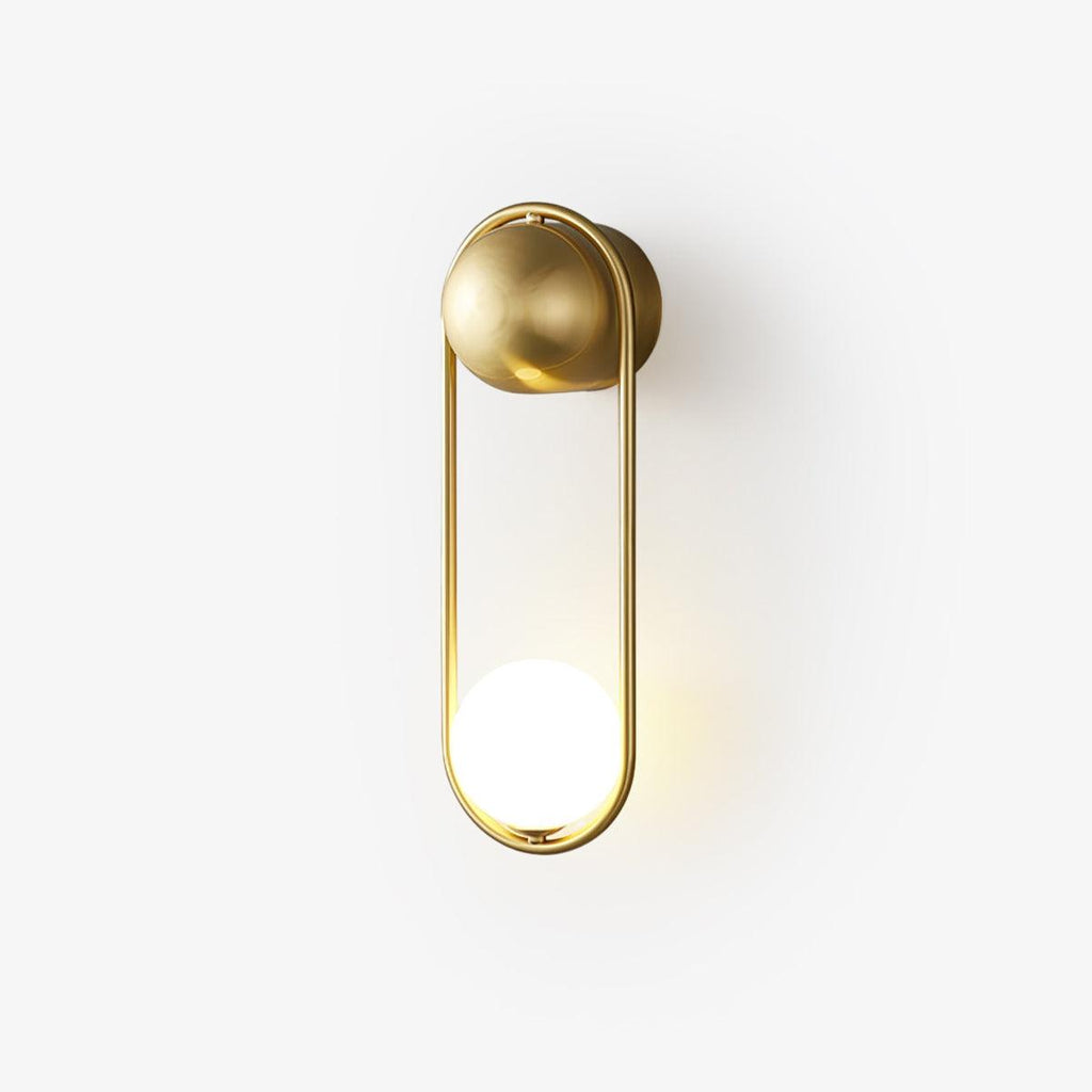 A brass Clérachic wall light on a plain white background, its opal glass globe glowing softly at the base.