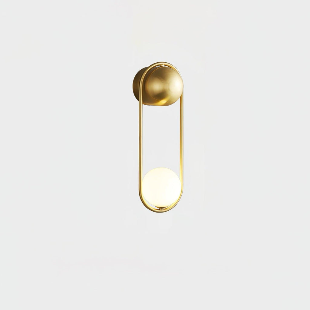 A brass Clérachic wall light on a plain white background, its opal glass globe glowing at the base of the loop.