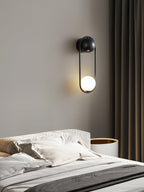 Above a patterned headboard beside dark curtains, this black-finish Clérachic wall light glows softly on a taupe wall.