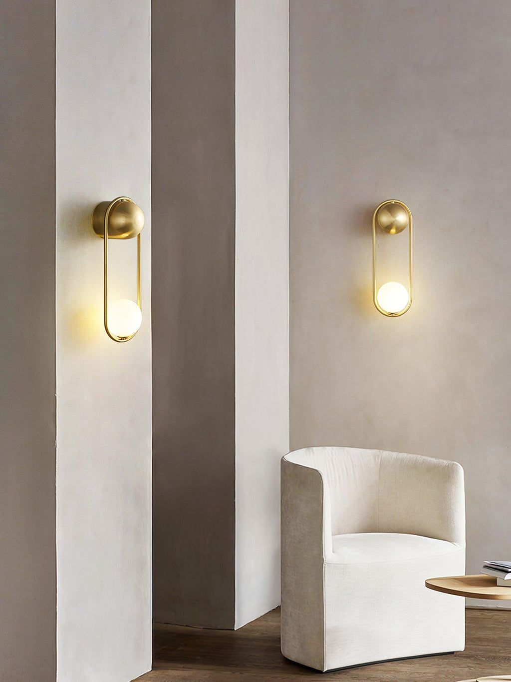 Two brass Clérachic wall lights sit on plaster pillars beside a cream armchair, shown unlit in daylight.