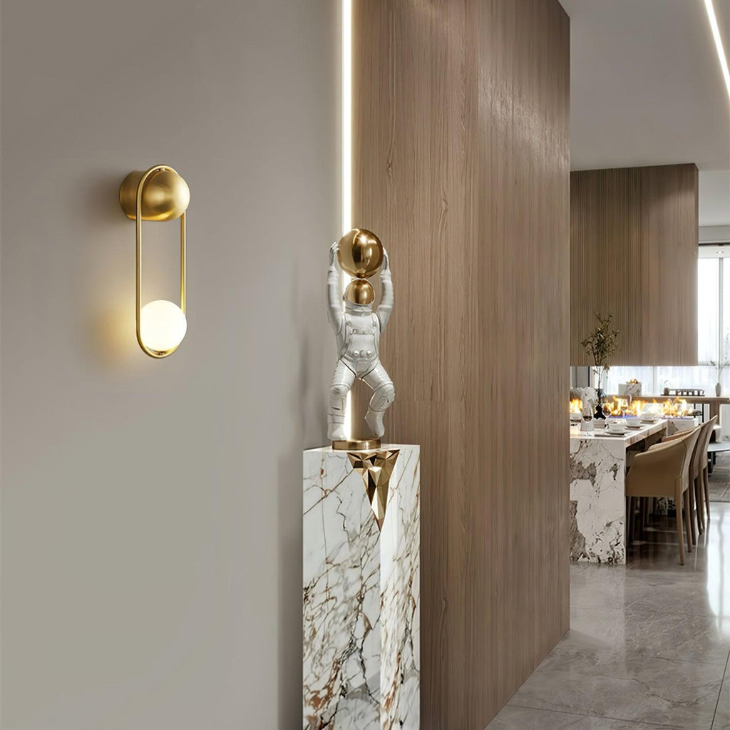 Beside a wood-panelled hallway with a marble plinth and small figurine, this brass Clérachic wall light sits near a dining area.