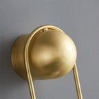 Extreme close-up of the brass ball top and curved loop on this Clérachic wall light against a plain grey wall.