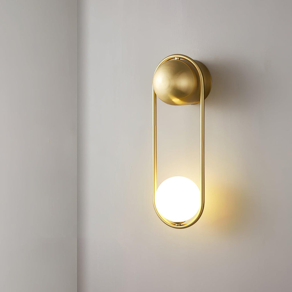 Side view of this brass Clérachic wall light on a plain wall, its opal glass globe lit at the base.