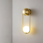 Side view of this brass Clérachic wall light on a plain wall, its opal glass globe lit at the base.