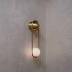 Close view of this brass Clérachic wall light on a limewashed plaster wall, its opal glass globe shown unlit.