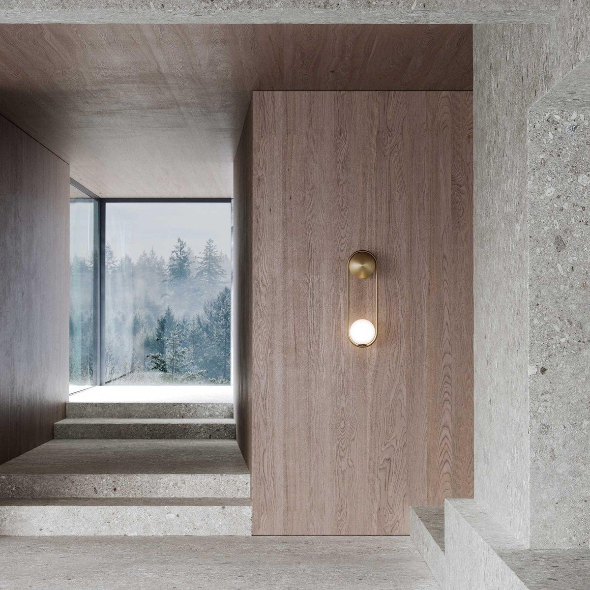 Beside a concrete stairwell with a window view of trees, this brass Clérachic wall light glows against a wood panel.