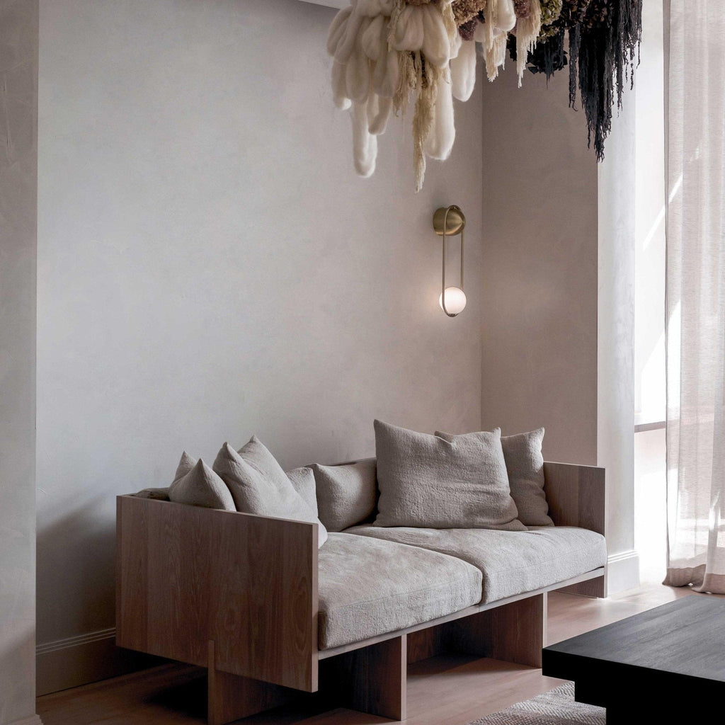 Seen across a living room with a sheer curtain and a hanging dried-flower display, this black-finish Clérachic wall light sits on a plain wall.