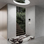 Beside an interior stairwell with greenery and a black-and-white marble step, this black-finish Clérachic wall light sits under a round skylight.