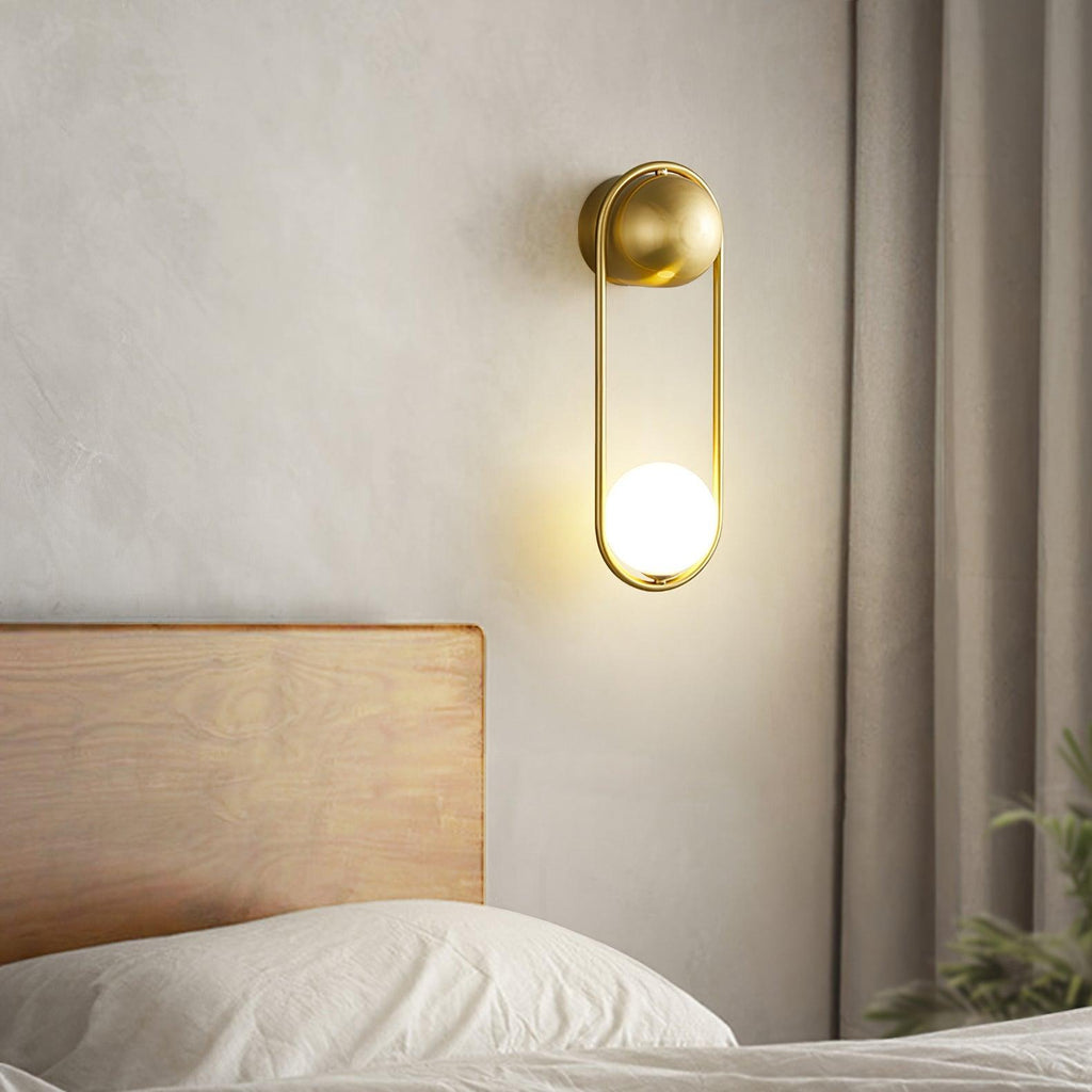 Mounted above a wooden headboard beside a sheer curtain, this brass Clérachic wall light glows warm against a beige wall.