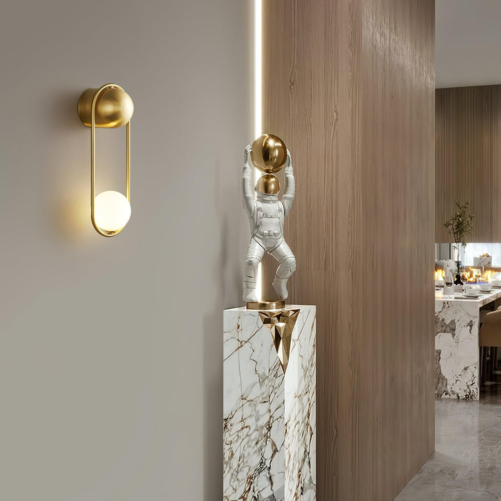 Beside a marble plinth with a small figurine in a wood-panelled hallway, this brass Clérachic wall light glows near a dining area.