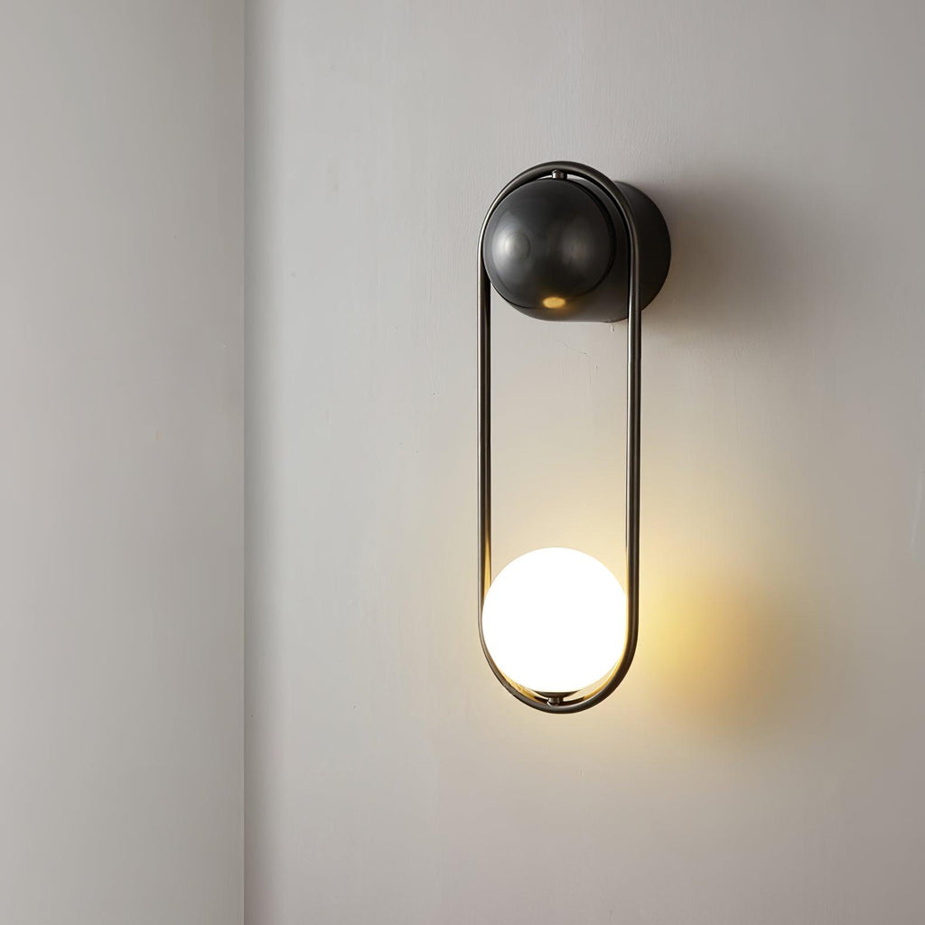 Close view of this black-finish Clérachic wall light on a plain wall, its opal glass globe glowing warm at the base.