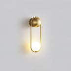 A brass Clérachic wall light on a plain grey background, its opal glass globe glowing at the base of the loop.