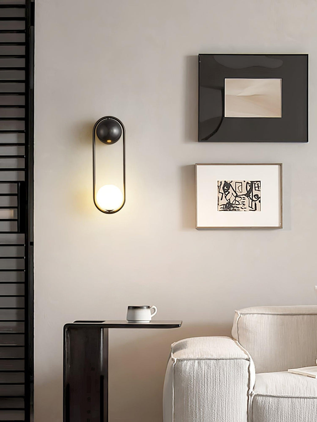 In a reading nook with a dark textured wall, framed art and a coffee cup on a side table, this black-finish Clérachic wall light glows.