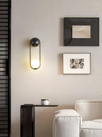 In a reading nook with a dark textured wall, framed art and a coffee cup on a side table, this black-finish Clérachic wall light glows.