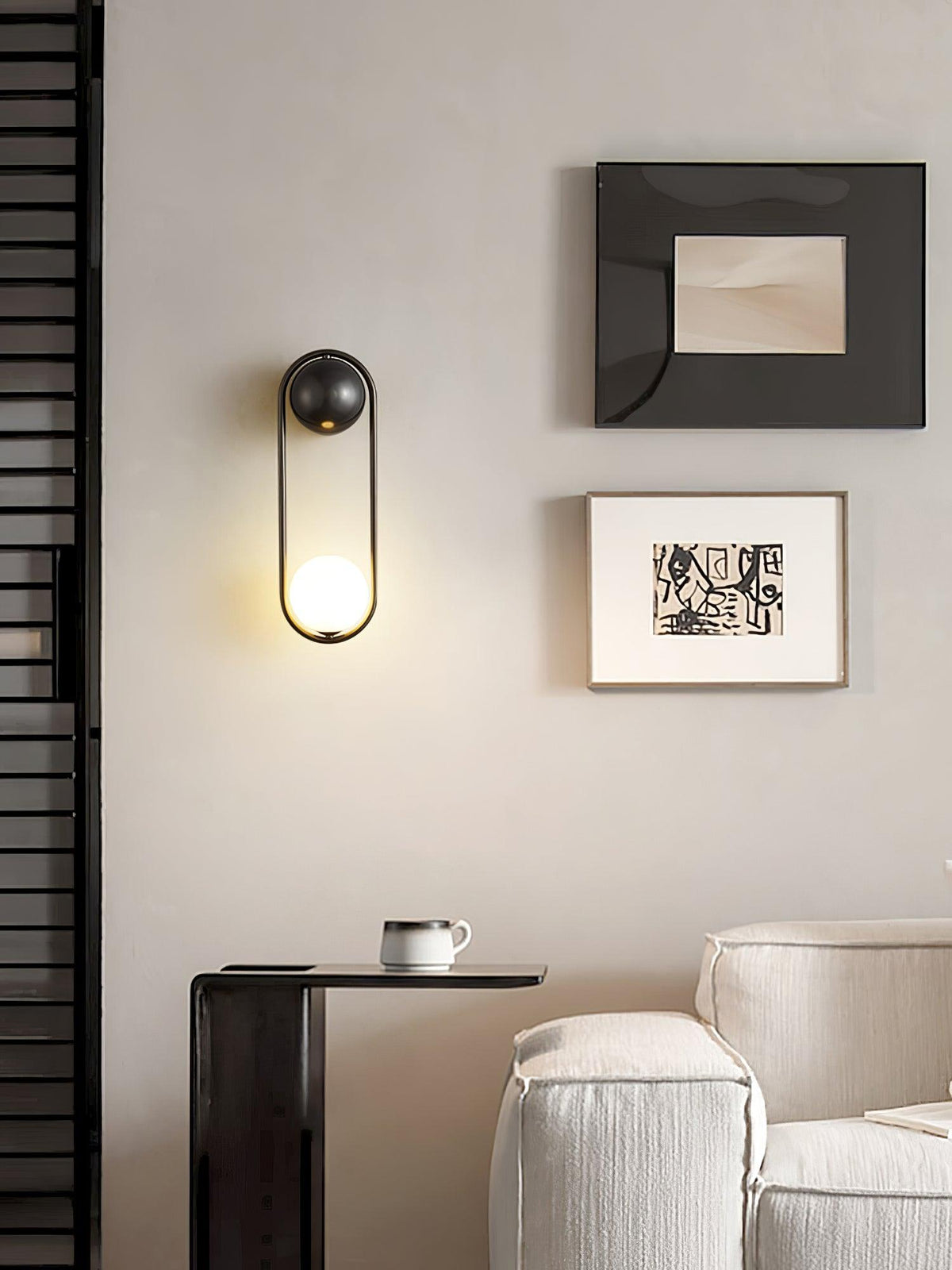 In a reading nook with a dark textured wall, framed art and a coffee cup on a side table, this black-finish Clérachic wall light glows.