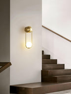 Beside a wooden staircase with a brass handrail, this brass Clérachic wall light glows against a plain wall.