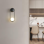 Beside a kitchen area with a marble counter and bar stools, this black-finish Clérachic wall light glows on a plain wall.