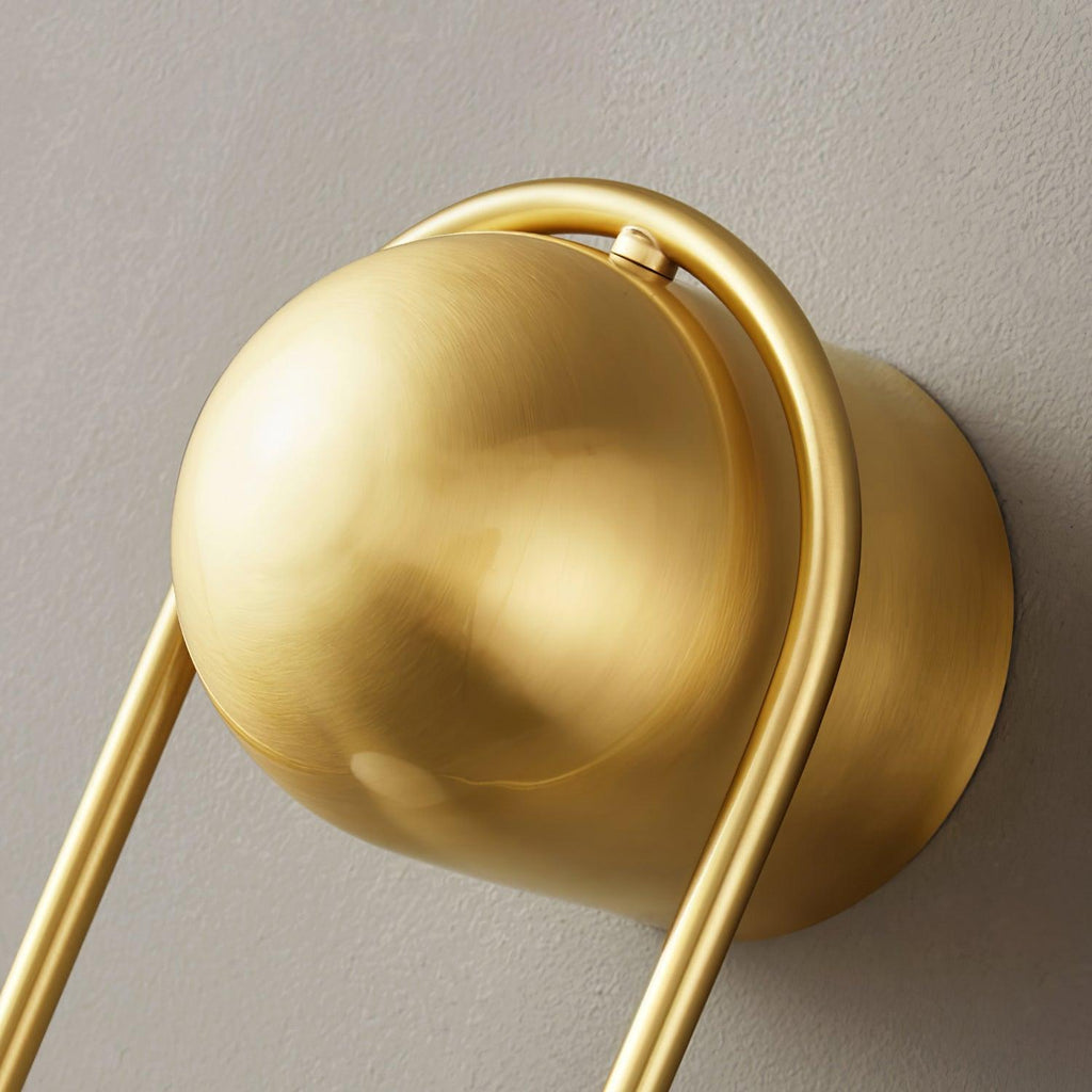 Close-up of the brass ball top and curved frame on this Clérachic wall light, seen from underneath against a plain wall.