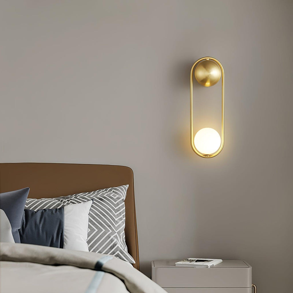 Above a camel-brown headboard beside a white nightstand with books, this brass Clérachic wall light glows softly.