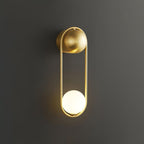 A brass Clérachic wall light on a dark charcoal background, its glass globe glowing warm at the base of the oval frame.