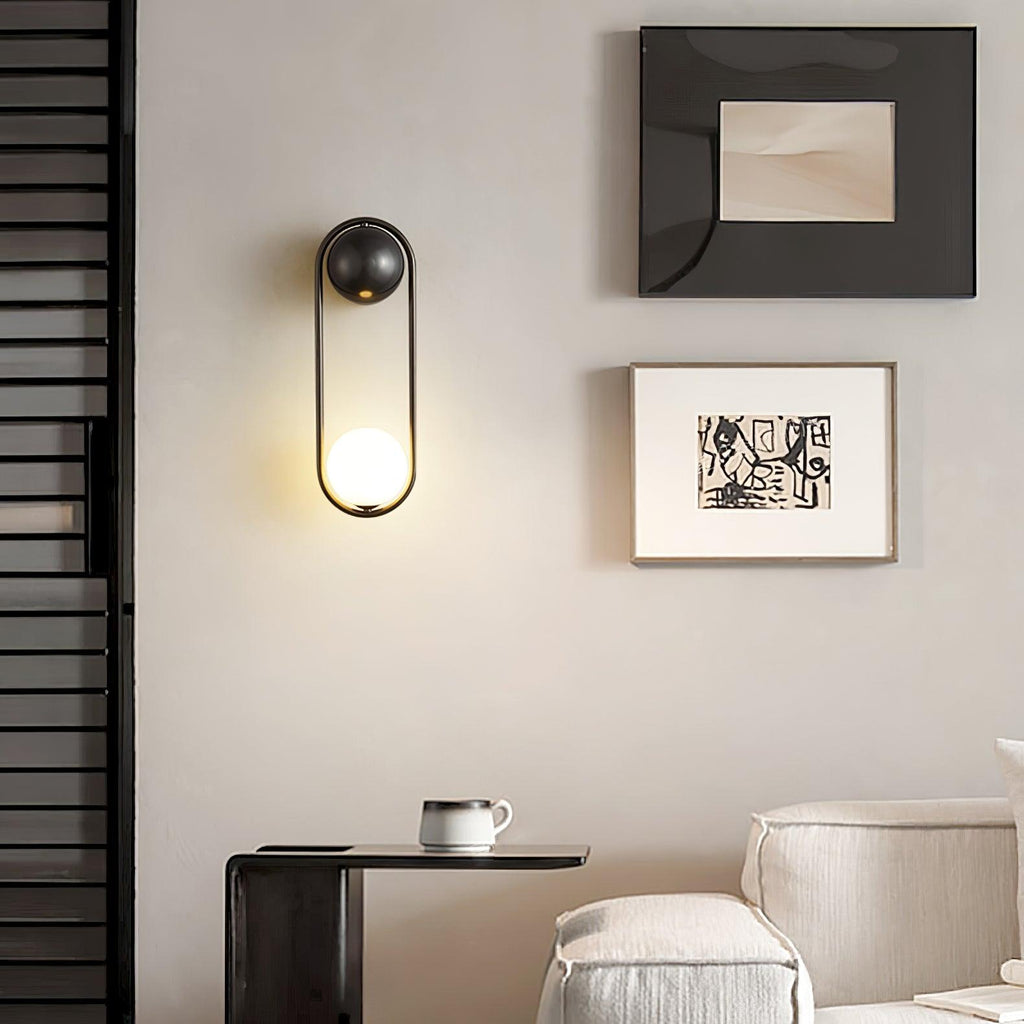 Beside a gallery of framed art and a small side table, this black-finish Clérachic wall light glows warm on a beige wall.