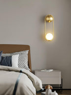 Above a camel-coloured headboard and a white nightstand, this brass Clérachic wall light glows softly on a taupe wall.