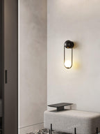 In a hallway nook near a closet door and an upholstered bench, this black-finish Clérachic wall light glows against a plain wall.