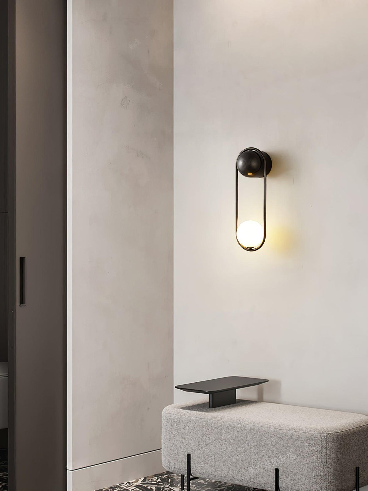 In a hallway nook near a closet door and an upholstered bench, this black-finish Clérachic wall light glows against a plain wall.