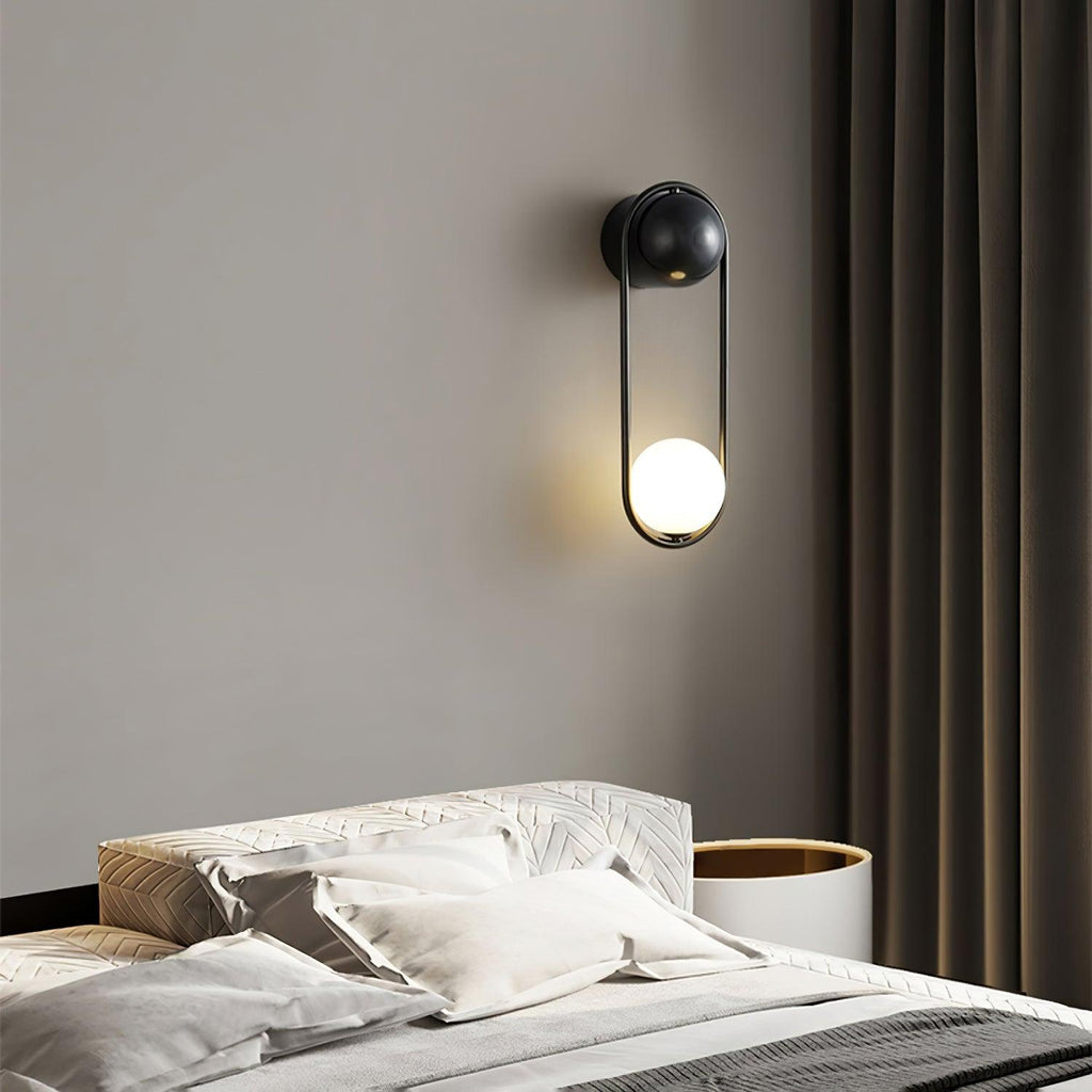 Mounted above a bed with a white and gold headboard and dark green curtains, this black-finish Clérachic wall light glows warm.