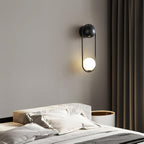 Mounted above a bed with a white and gold headboard and dark green curtains, this black-finish Clérachic wall light glows warm.