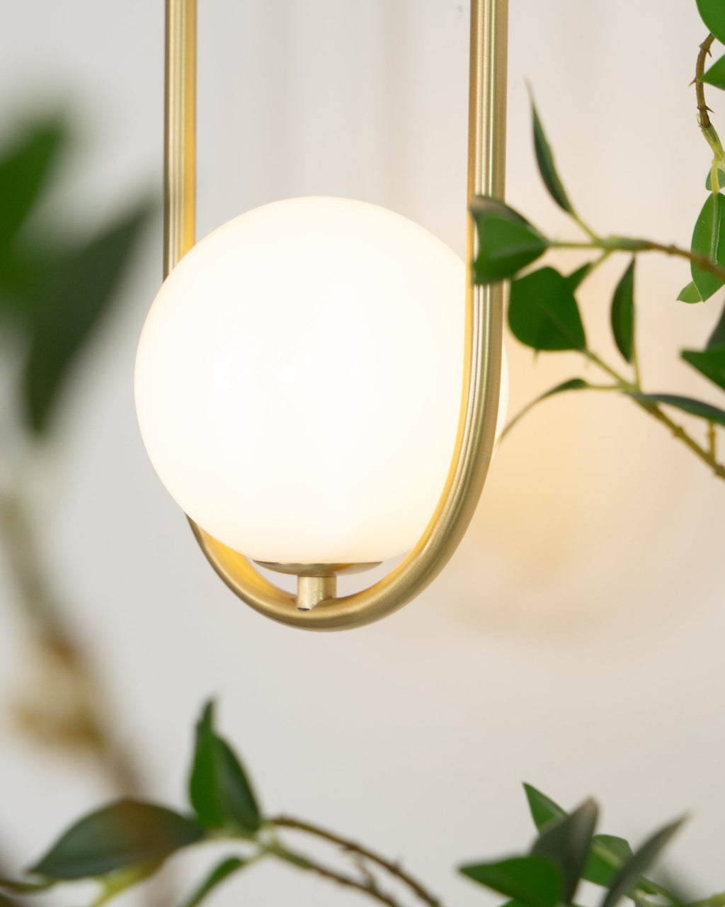 Extreme close-up of the glowing opal glass globe on this Clérachic wall light, framed by green leaves.