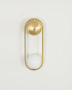A brass Clérachic wall light on an off-white background, its opal glass globe shown unlit inside the oval frame.