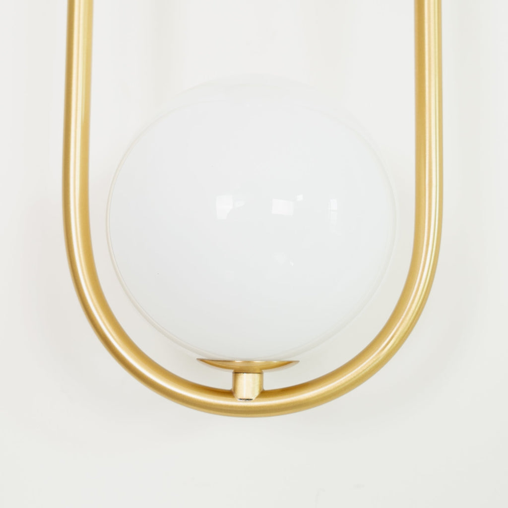 Extreme close-up of the large opal glass globe inside the brass loop on this Clérachic wall light, shown unlit.