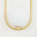 Extreme close-up of the large opal glass globe inside the brass loop on this Clérachic wall light, shown unlit.