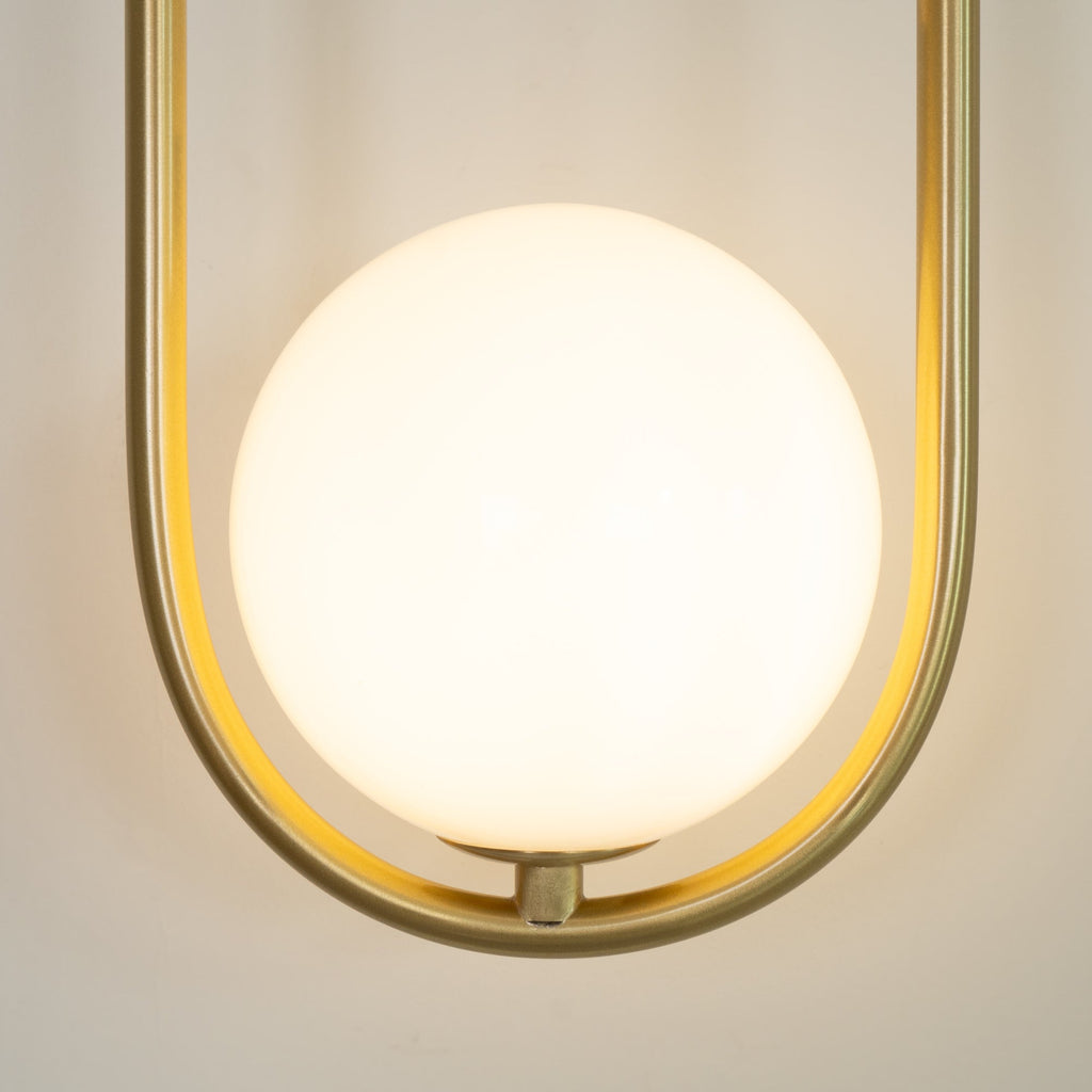 Close-up of the opal glass globe glowing warm inside the brass loop on this Clérachic wall light.