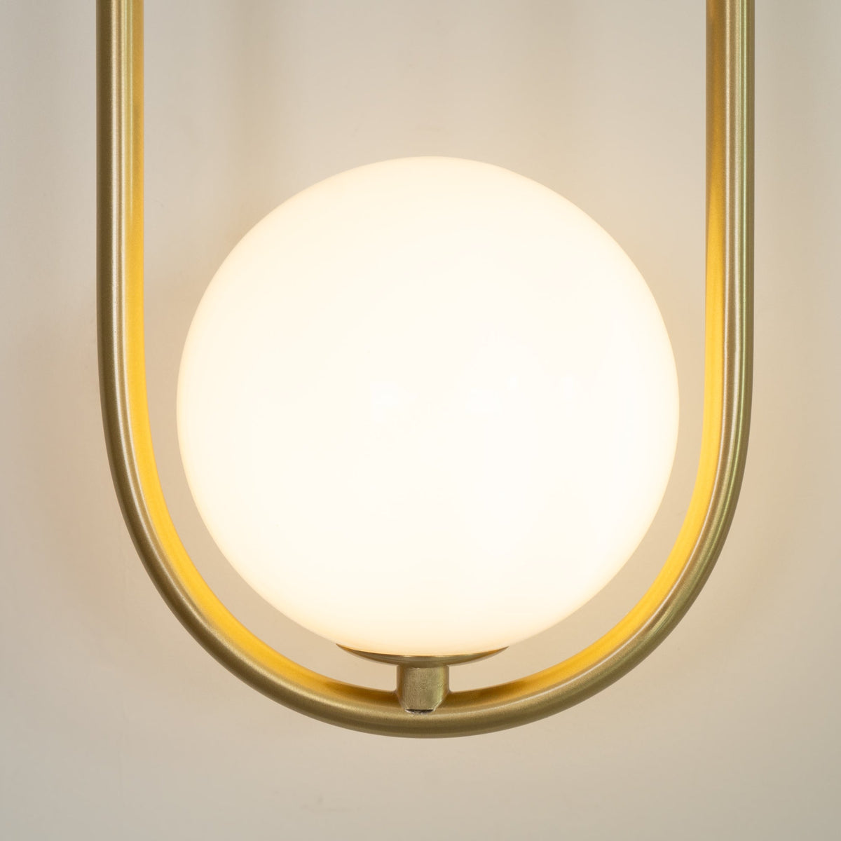 Close-up of the opal glass globe glowing warm inside the brass loop on this Clérachic wall light.