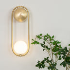 Beside trailing green leaves, this brass Clérachic wall light glows softly on a plain wall.